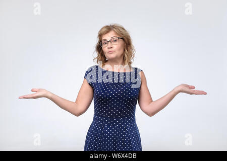 Perplesso femmina matura in vestito blu alza le spalle spalle come non sa rispondere, Foto Stock