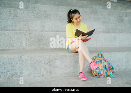 Ragazza adolescente legge un libro su scala nel pomeriggio. Studentessa a studiare per esame nel campus. Foto Stock