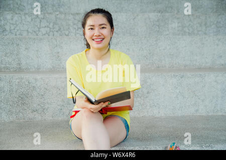 Ragazza adolescente legge un libro su scala nel pomeriggio. Studentessa a studiare per esame nel campus. Foto Stock