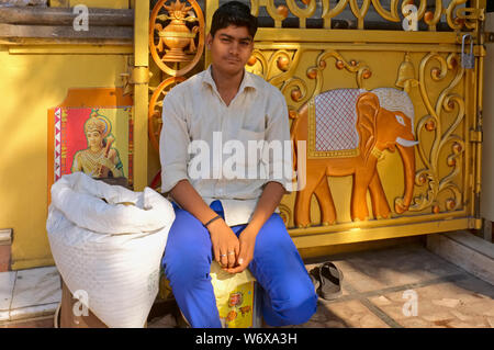 Un giovane da migranti Uttar Pradesh N.India si siede di fronte a un ornato di Temple Gate in Mumbai, India, disegnato da Mumbai della ricchezza di opportunità di lavoro Foto Stock