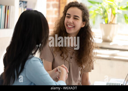 Giovani donne seduti alla scrivania sorridente agitare le mani Foto Stock