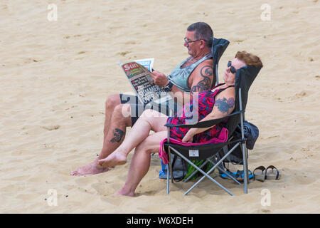 Bournemouth, Dorset Regno Unito. 3 agosto 2019. Regno Unito tempo: overcast e nuvoloso, ma caldo e muggy. I Beach Goers si dirigono verso le spiagge di Bournemouth per godersi il tempo caldo. Coppia rilassante in sedie sulla spiaggia, uomo che legge il giornale Sun. Credit: Carolyn Jenkins/Alamy Live News Foto Stock