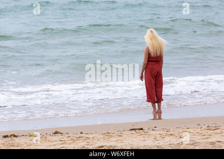 Bournemouth, Dorset Regno Unito. 3 agosto 2019. Regno Unito tempo: overcast e nuvoloso, ma caldo e muggy. I Beach Goers si dirigono verso le spiagge di Bournemouth per godersi il tempo caldo. Donna in piedi sul mare remare in mare - vista posteriore vista posteriore. Credit: Carolyn Jenkins/Alamy Live News Foto Stock