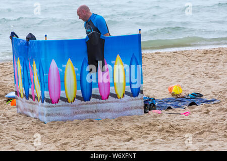 Bournemouth, Dorset Regno Unito. 3 agosto 2019. Regno Unito tempo: overcast e nuvoloso, ma caldo e muggy. I Beach Goers si dirigono verso le spiagge di Bournemouth per godersi il tempo caldo. Uomo dietro vento break break. Credit: Carolyn Jenkins/Alamy Live News Foto Stock