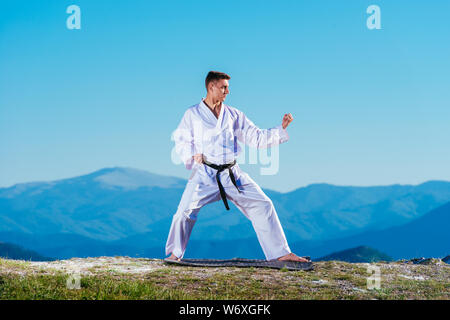 Bionda atleta di karate non kata sulla cima di una montagna mentre si esegue una linea di calci, pugni e blocchi sulla cima di una montagna in una giornata di sole. Foto Stock