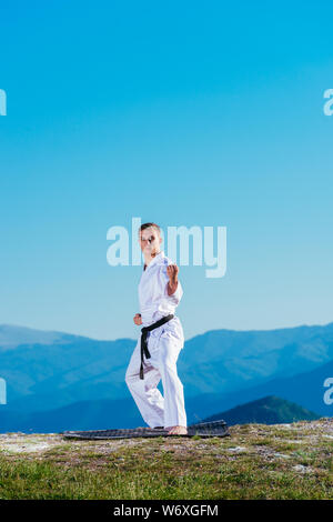 Bionda atleta di karate non kata sulla cima di una montagna mentre si esegue una linea di calci, pugni e blocchi sulla cima di una montagna in una giornata di sole. Foto Stock