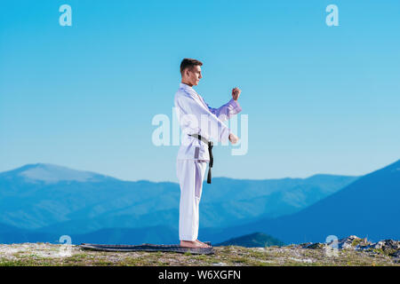 Bionda atleta di karate non kata sulla cima di una montagna mentre si esegue una linea di calci, pugni e blocchi sulla cima di una montagna in una giornata di sole. Foto Stock