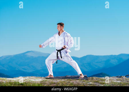 Bionda atleta di karate non kata sulla cima di una montagna mentre si esegue una linea di calci, pugni e blocchi sulla cima di una montagna in una giornata di sole. Foto Stock