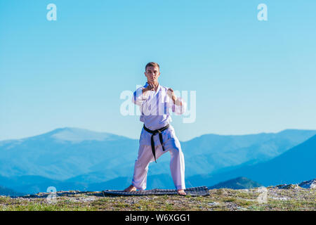 Bionda atleta di karate non kata sulla cima di una montagna mentre si esegue una linea di calci, pugni e blocchi sulla cima di una montagna in una giornata di sole. Foto Stock