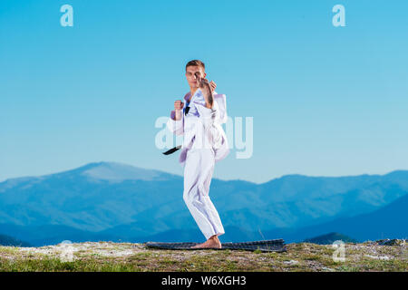 Bionda atleta di karate non kata sulla cima di una montagna mentre si esegue una linea di calci, pugni e blocchi sulla cima di una montagna in una giornata di sole. Foto Stock