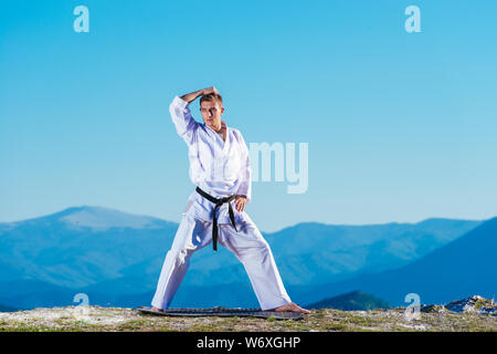 Bionda atleta di karate non kata sulla cima di una montagna mentre si esegue una linea di calci, pugni e blocchi sulla cima di una montagna in una giornata di sole. Foto Stock