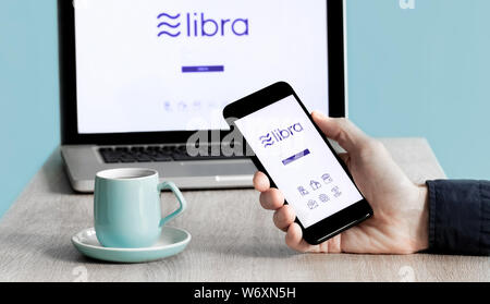 Maschio caucasico mano utilizzando Facebook Libra Crypto valuta digitale App su smartphone e computer portatile Foto Stock