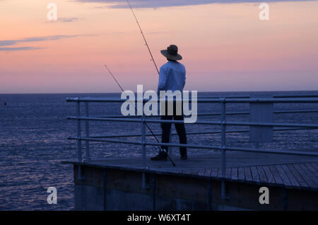 CATTURE mattutine: Un uomo prende in qualche mattina pesca poco prima dell'alba su un molo fuori dalla baia di Absecon nella città atlantica, New Jersey. Foto Stock
