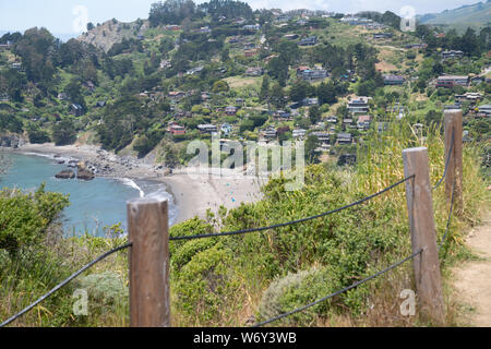 In legno e recinto di filo con la spiaggia cittadina con le case sulla collina accanto a Ocean Foto Stock