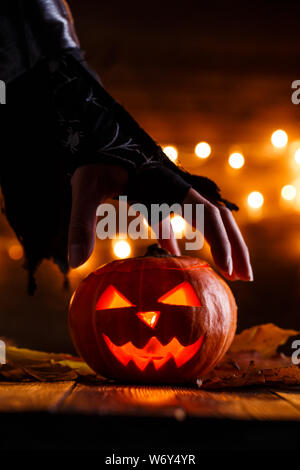 Immagine di sfondo di halloween con zucca e strega mano sul tavolo di legno contro il grunge bokeh sfondo luci Foto Stock