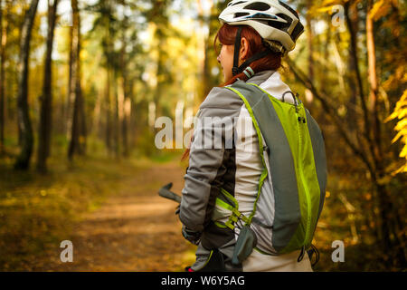 Foto di donna sorridente indossando il casco e abbigliamento sportivo in bicicletta nella foresta di autunno Foto Stock