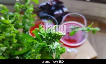 Vista dall'alto di due bicchieri con un rosso cocktail rinfrescante decorato con foglie di menta su uno sfondo di mazzetti di menta e basilico viola, il fuoco selettivo Foto Stock