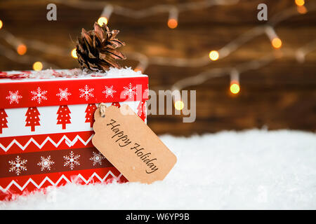 Rosso scatola di Natale e tag di carta sulla neve e scuro dello sfondo in legno Foto Stock