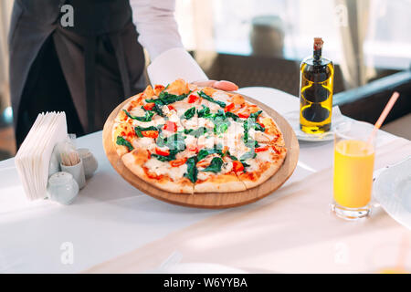 Il cameriere pizza mette sul tavolo del ristorante. Foto Stock