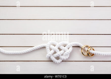 A forma di cuore di corde e di un doppio anello oro bianco su sfondo di legno Foto Stock