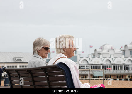 Due anziane signore o donne seduto su una panchina a parlare in inglese mare Foto Stock