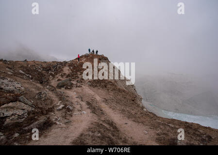 Gruppo di turisti standng su una scogliera sovrastante Ghiacciaio piscine e scenari montuosi in Himalaya. Nebbia fitta, visibile a fiocchi di neve. Foto Stock