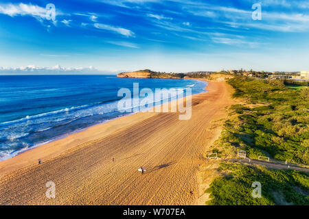 Le onde di laminazione a Mona Vale beach con surfers camminare su ampia spiaggia di sabbia con le schede per ottenere il surf in cristalline acque dell'Oceano Pacifico. Foto Stock