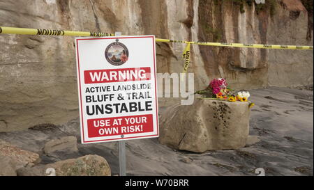 Segni e nastro di avvertenza avvisa di scogliere instabili al Grandview Beach in Encinitas - sito di un letale bluff crollo. I fiori piangono i morti beachgoers. Foto Stock