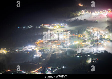 La nebbia che fluisce in un piccolo villaggio e gli alberi nei pressi del Monte Bromo di notte Foto Stock