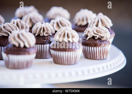 Vassoio di tortini di cioccolato con girandola di glassa sulla parte superiore di colore bianco porcellana portagiornali Foto Stock