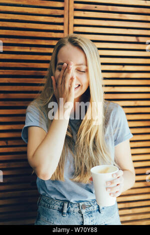 La ragazza ride e si copre la faccia con la sua mano, emozioni naturali Foto Stock