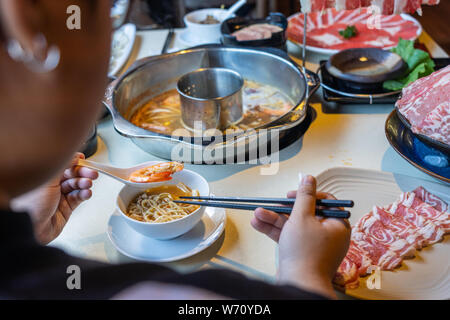 Donna con bacchette e cucchiaio di mangiare in stile asiatico hotpot frutti di mare Foto Stock