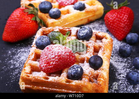 In casa tradizionale cialde belghe con frutta fresca, frutti di bosco e zucchero in polvere sulla piastra nera Foto Stock