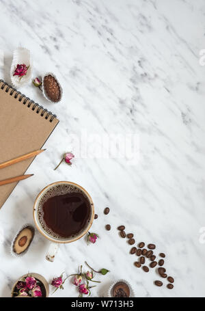 Composizione di mattina con una tazza di caffè nero, cioccolatini e un portatile su una superficie in marmo con spazio per testo, vista dall'alto Foto Stock