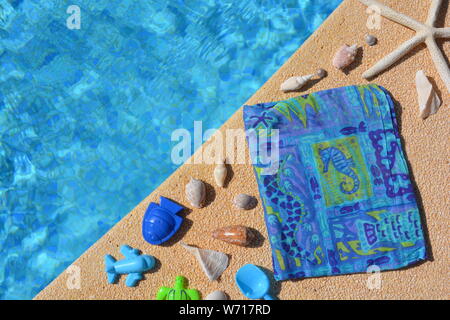 Il flip flop, conchiglie, spiaggia wrap e giocattolo aereo blu in corrispondenza del bordo di una piscina. Piatto estivo lay, concetto creativo. Foto Stock