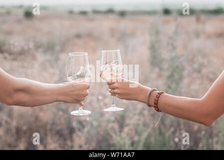 Due bicchieri di vino rosa nelle donne le mani sul tramonto picnic. Close up. Foto Stock