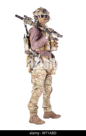 Appassionato di Strikeball in camicia a scacchi con munizioni militari, maschera facciale, casco e cuffie radio, occhiali tattici, pantaloni camo, fucile da servizio armato e sparare in studio con pistola isolato su bianco Foto Stock