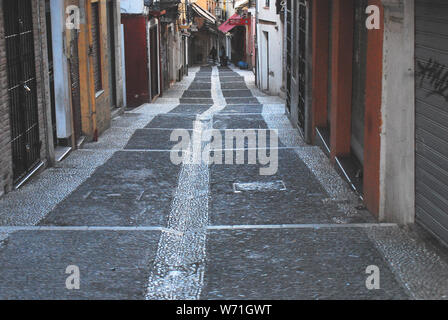 Un wet, strette down hill street foderato con Colorati luminosamente edifici, nel centro della splendida Granada, Spagna. Foto Stock