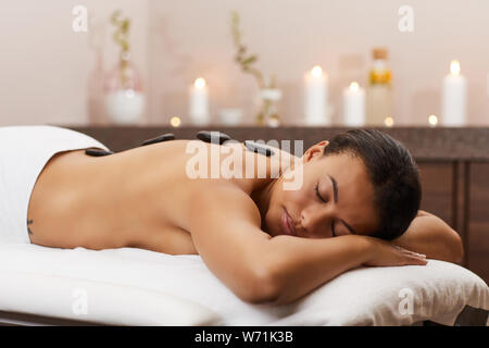 Vista laterale ritratto della bella mixed-gara donna disteso sul lettino da massaggio durante la terapia di pietra nel centro termale, spazio di copia Foto Stock
