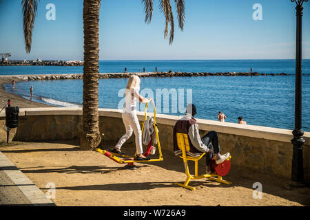 Novembre 21, 2017 - MARBELLA, Spagna. Le persone che usano il pubblico esercizio macchine in una giornata di sole accanto alla spiaggia. Cielo blu e il mare mediterraneo dietro. Foto Stock