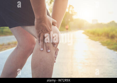 Pregiudizio dal concetto di allenamento : l'uomo asiatico di usare le mani tenere sul suo ginocchio durante il funzionamento su strada nel parco. Girato in mattinata il tempo, la luce del sole e caldo effe Foto Stock