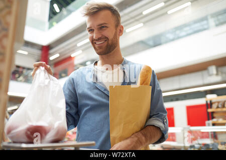 Vita ritratto di bel giovane del peso di verdure nel supermercato e sorridente al cassiere, spazio di copia Foto Stock