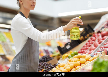 Vista laterale Ritratto di giovane donna la spruzzatura di acqua su frutta e verdura fresca stabilite per la vendita al mercato degli agricoltori, spazio di copia Foto Stock