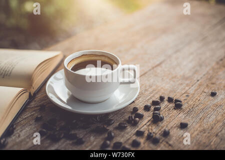 Bianco di ceramica tazza da caffè di nero caldo americano sul tavolo di legno o un contatore con libro Foto Stock