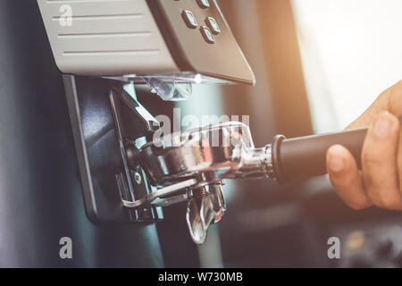 Mano del barista tenendo la maniglia di caffè e rendendo la macinazione del caffè appena tostato chicchi di caffè con macchina automatica Foto Stock