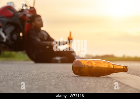 Motociclista seduto sulla strada accanto alla sua moto e bere un alcol o birra. Di sicuro ride concept Foto Stock