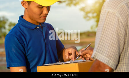 Uomo di consegna azienda marrone o pacchi di scatole di cartone e la consegna al cliente in campagna e la vista del campo di riso. Può essere la consegna ovunque conce Foto Stock