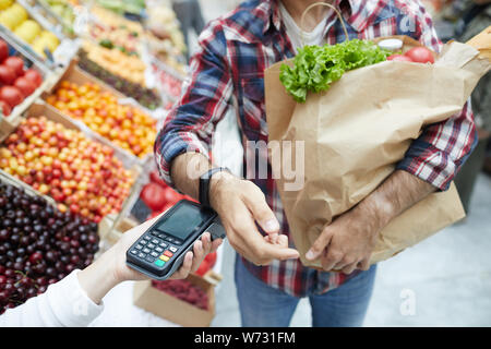 Primo piano di un irriconoscibile uomo pagando tramite smartwatch mentre la spesa al mercato degli agricoltori, spazio di copia Foto Stock