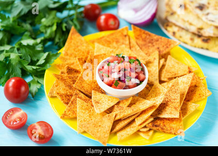 Il mais tortilla chips Nachos con la paprika e salsa di pomodoro sulla piastra, sfondo blu. Tradizionale cibo messicano Tex Mex Foto Stock