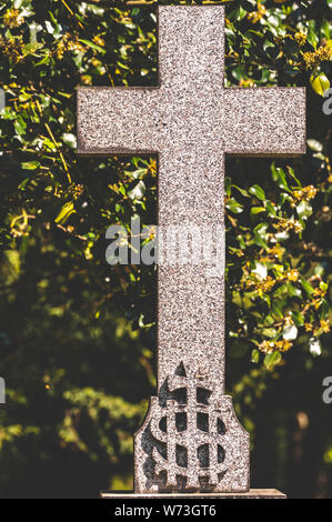 Immagine opaca di una croce in marmo con il monogramma IHS sul fondo e alberi dietro. IHS è chiamato un Chrisotgram e si basa su un antico modo di scrittura di Gesù Cristo. Foto Stock